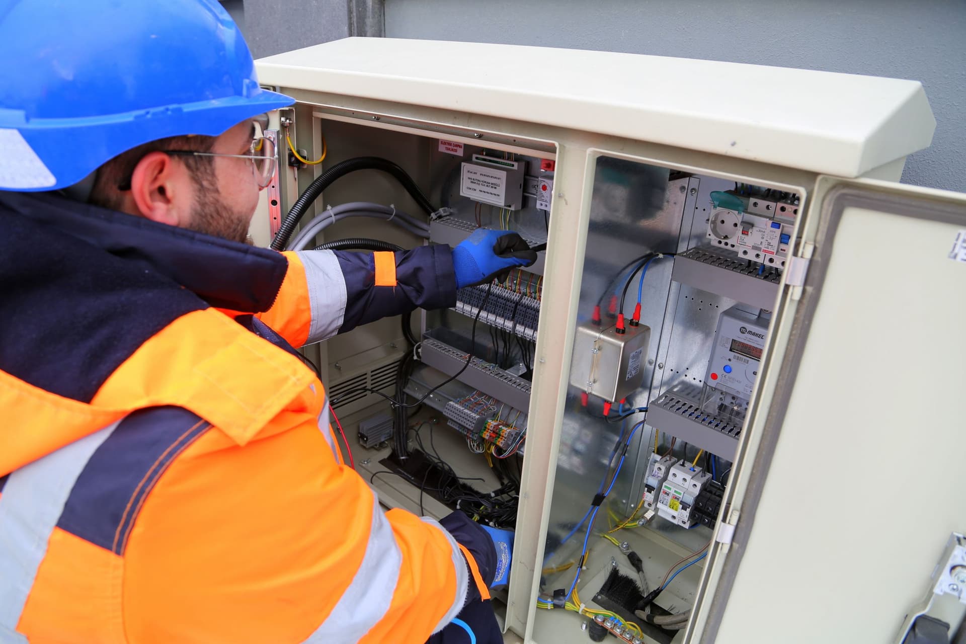 Electrician in a hard hat and hi-vis working on an electrical cabinet