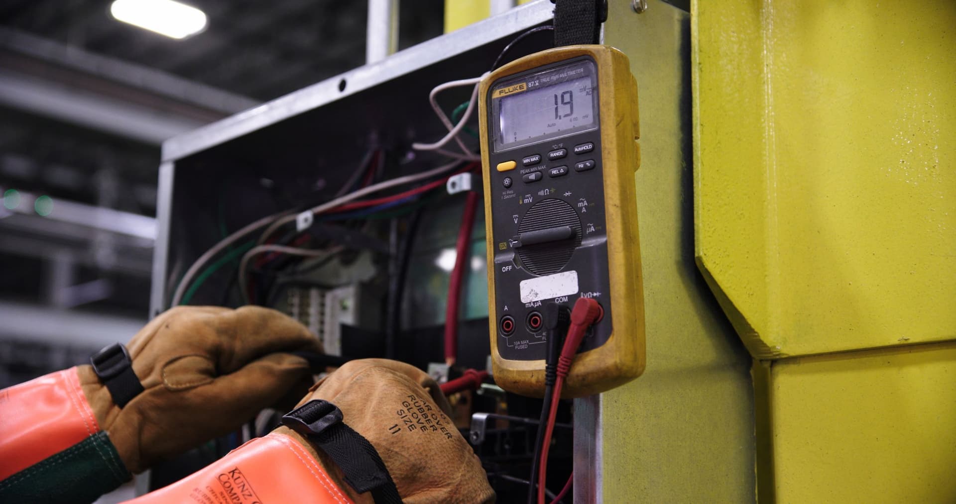 Electrician in insulated gloves taking a multimeter reading in a control panel
